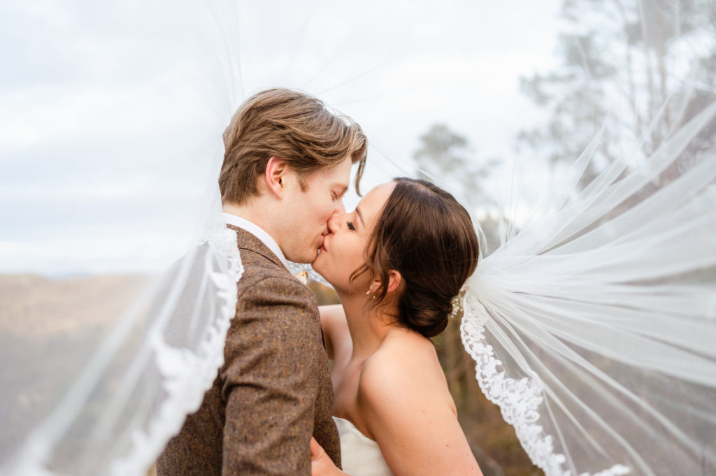 Brudepar kysser med brudeslør som flyr mot kamera.
