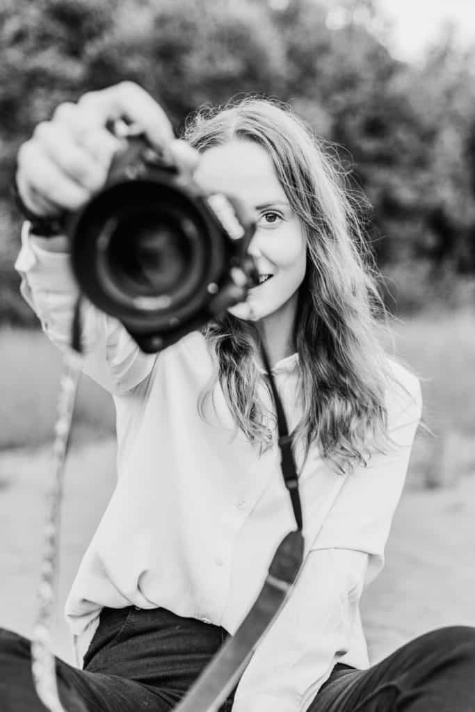 Fotograf Anne Katja Gaup sitter på bakken og holder opp kamera. 