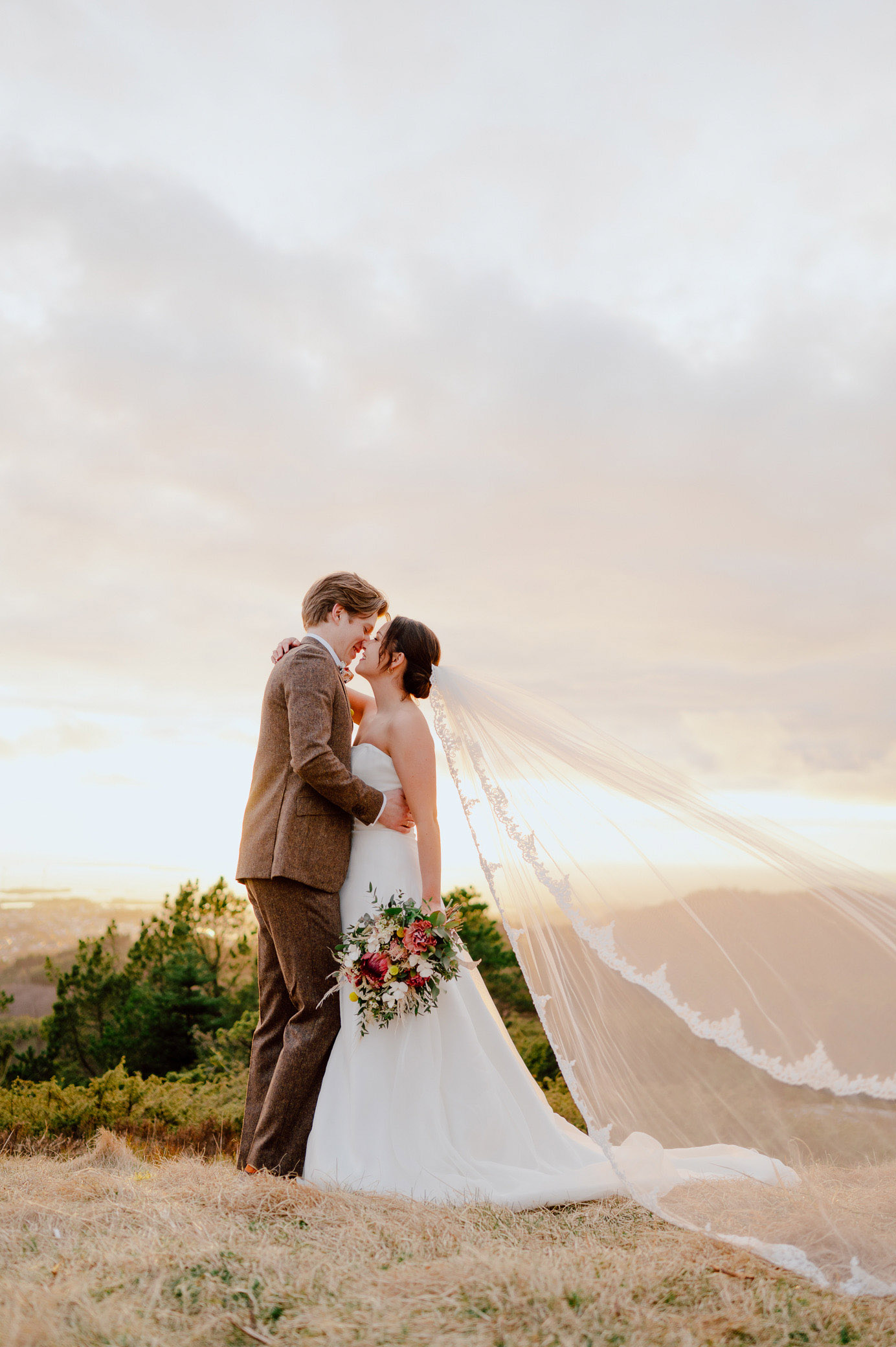 Brudepar kysser i solnedgang på et fjell.